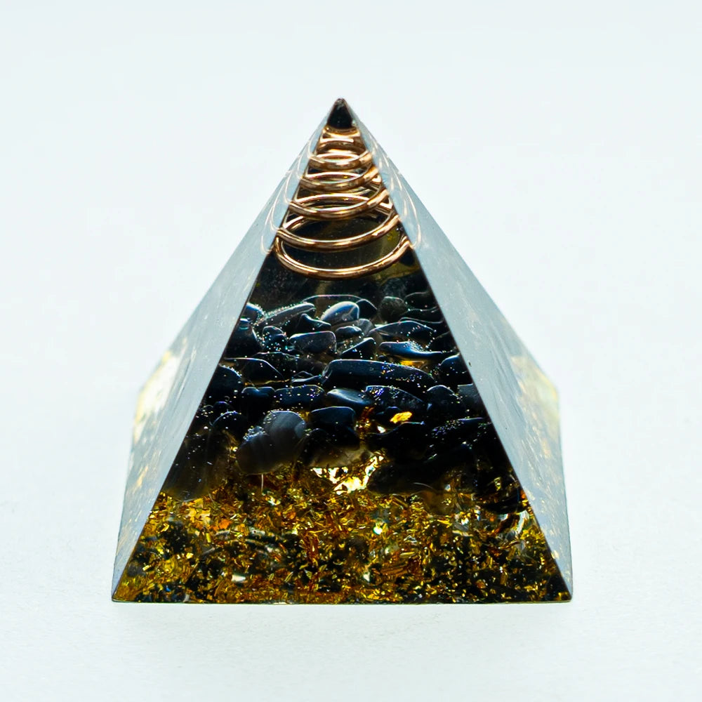 A clear pyramid-shaped crystal containing dark stones and a coiled copper wire, used for Reiki and meditation.