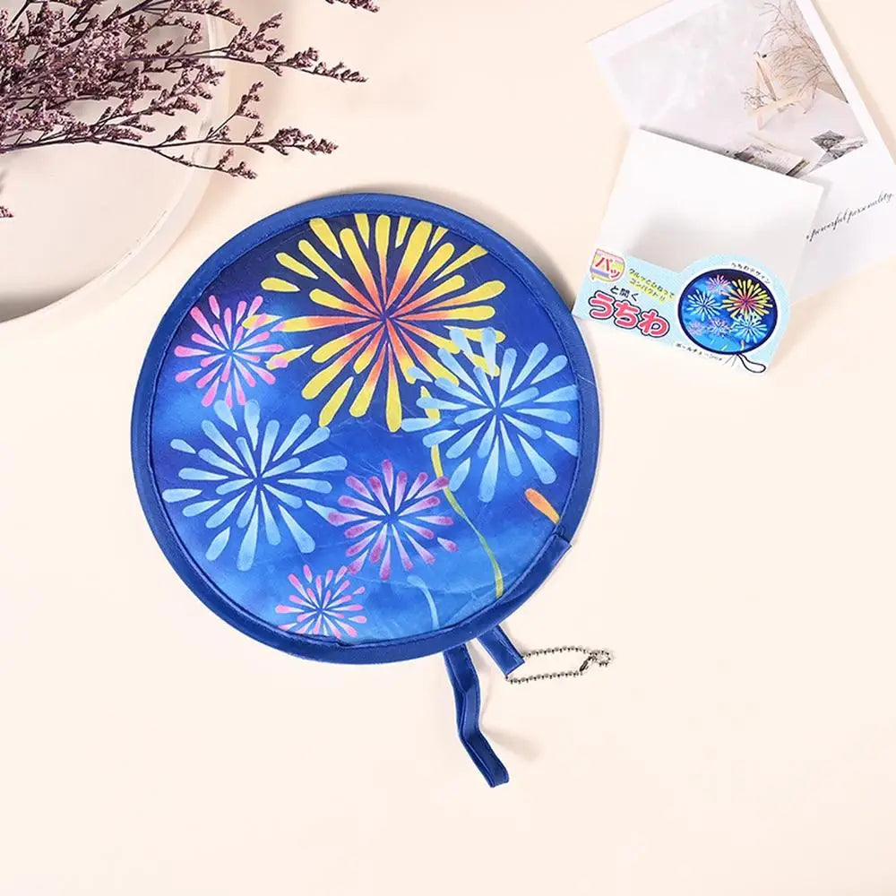 A blue fabric fan with a yellow and purple floral design is shown next to some paper and dried flowers.