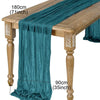 A teal gauze table runner draped over a wooden table, showing its texture and length.