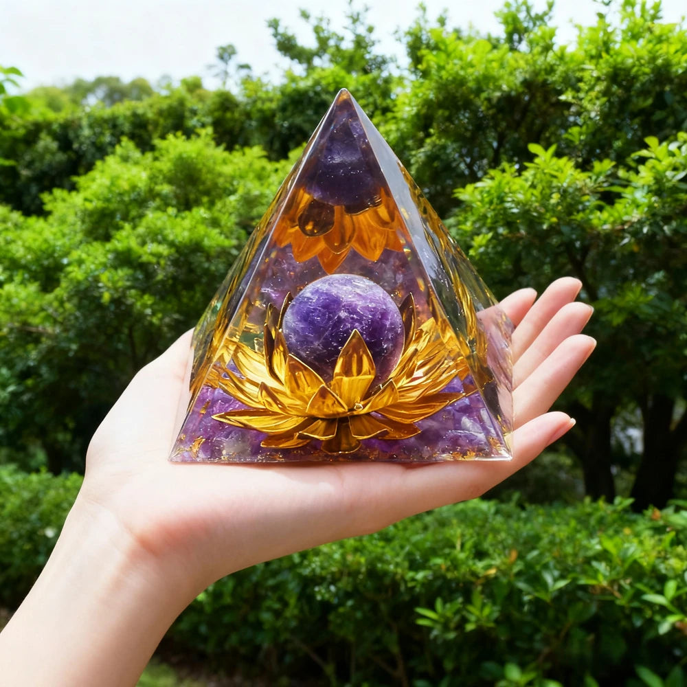 Hand holding a clear resin pyramid with purple obsidian and a gold copper coil set against a green outdoor background