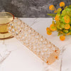 A long, cylindrical crystal gold flower vase with a textured pattern is displayed on a white marble surface.