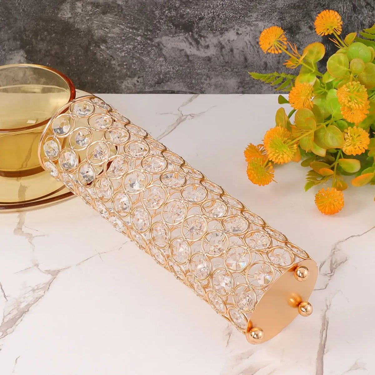 A long, cylindrical crystal gold flower vase with a textured pattern is displayed on a white marble surface.
