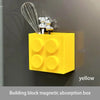 Yellow building block magnetic absorption box with silver whisk and gold-colored charms mounted on a gray wall.