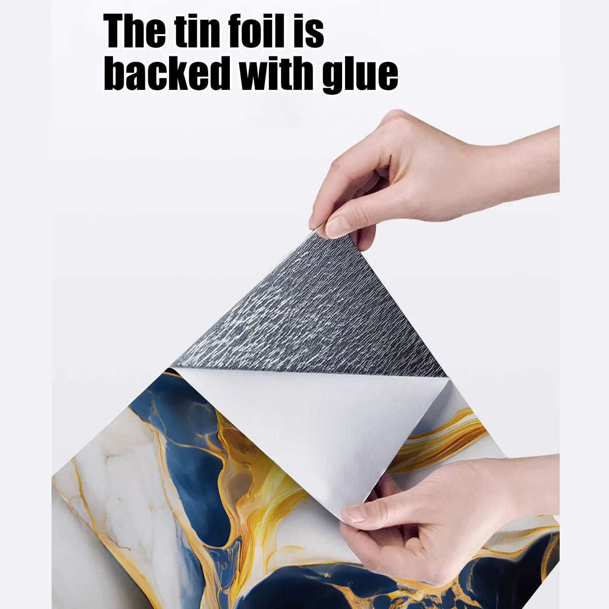 A hand is peeling a tin foil backing from a piece of faux marble wallpaper, revealing the textured surface.