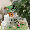 A white birthday cake decorated with soccer players, field elements, and a happy birthday topper.