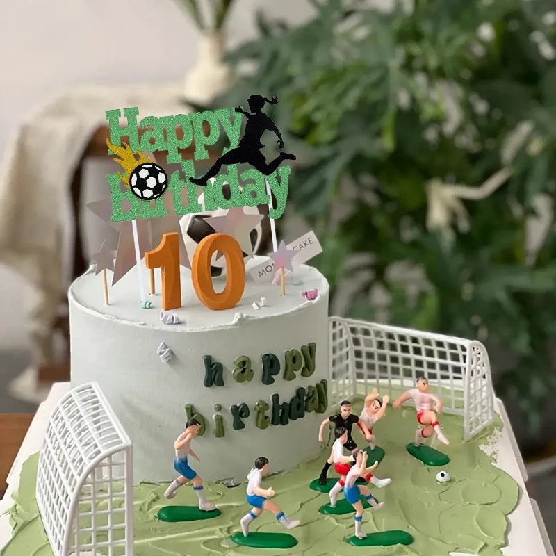 A white birthday cake decorated with soccer players, field elements, and a happy birthday topper.