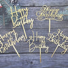 Gold acrylic birthday cake toppers with happy birthday lettering on a dark wooden background