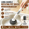 A hand is using a long-handled rotating pot brush with a liquid dispenser to clean a pot.