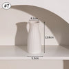 A white, ribbed ceramic vase is displayed on a shelf with a shadow cast behind it.