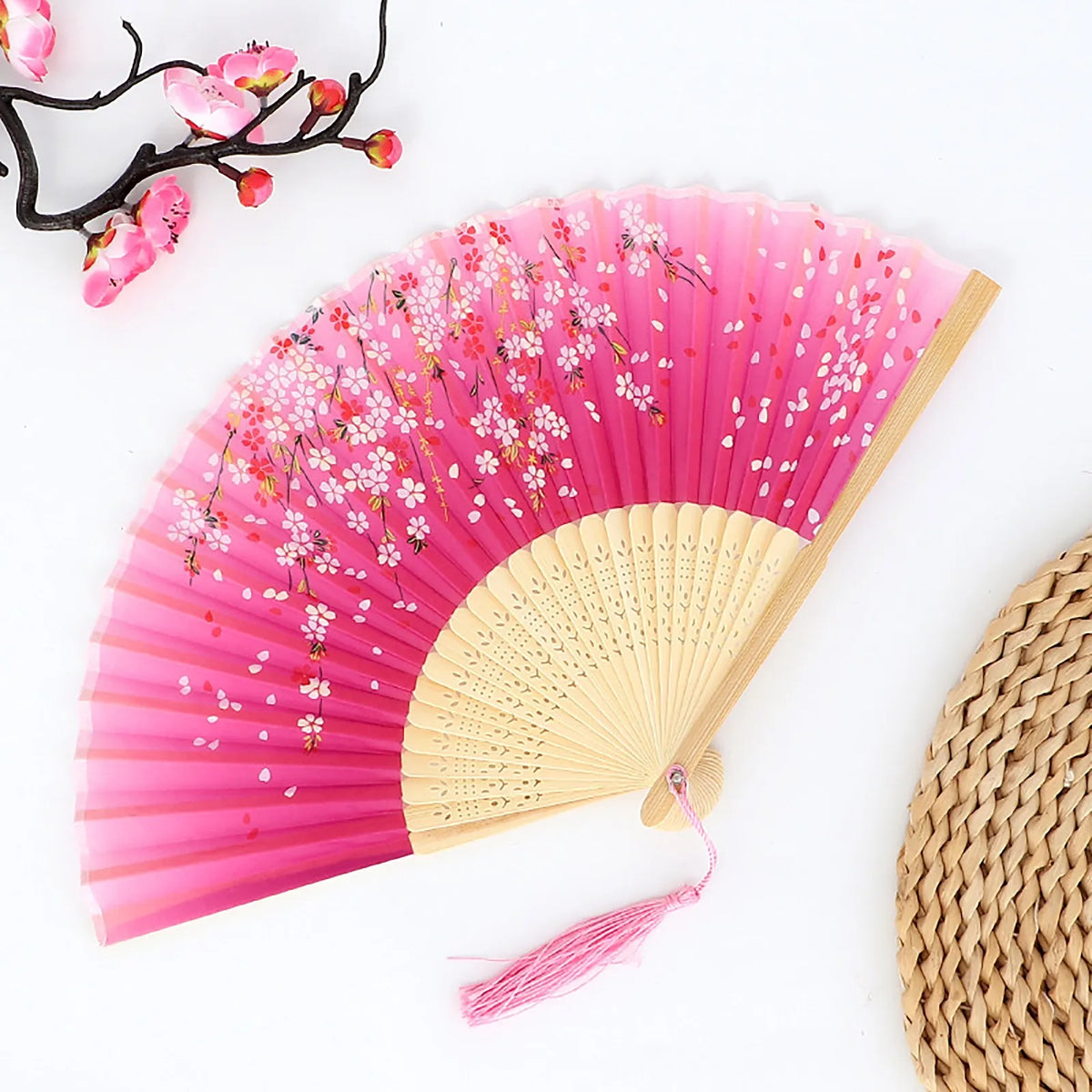 Pink folding fan with color-changing fabric and cherry blossom designs against a white background.