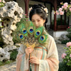 Une femme tient un éventail à plumes de paon naturel de style traditionnel à l'extérieur.