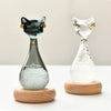 A glass bottle shaped like an Egyptian cat with gold accents and filled with ice on a wooden base.