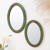 A vintage olive green oval wall mirror with an intricate gold lace design hanging on a white surface.