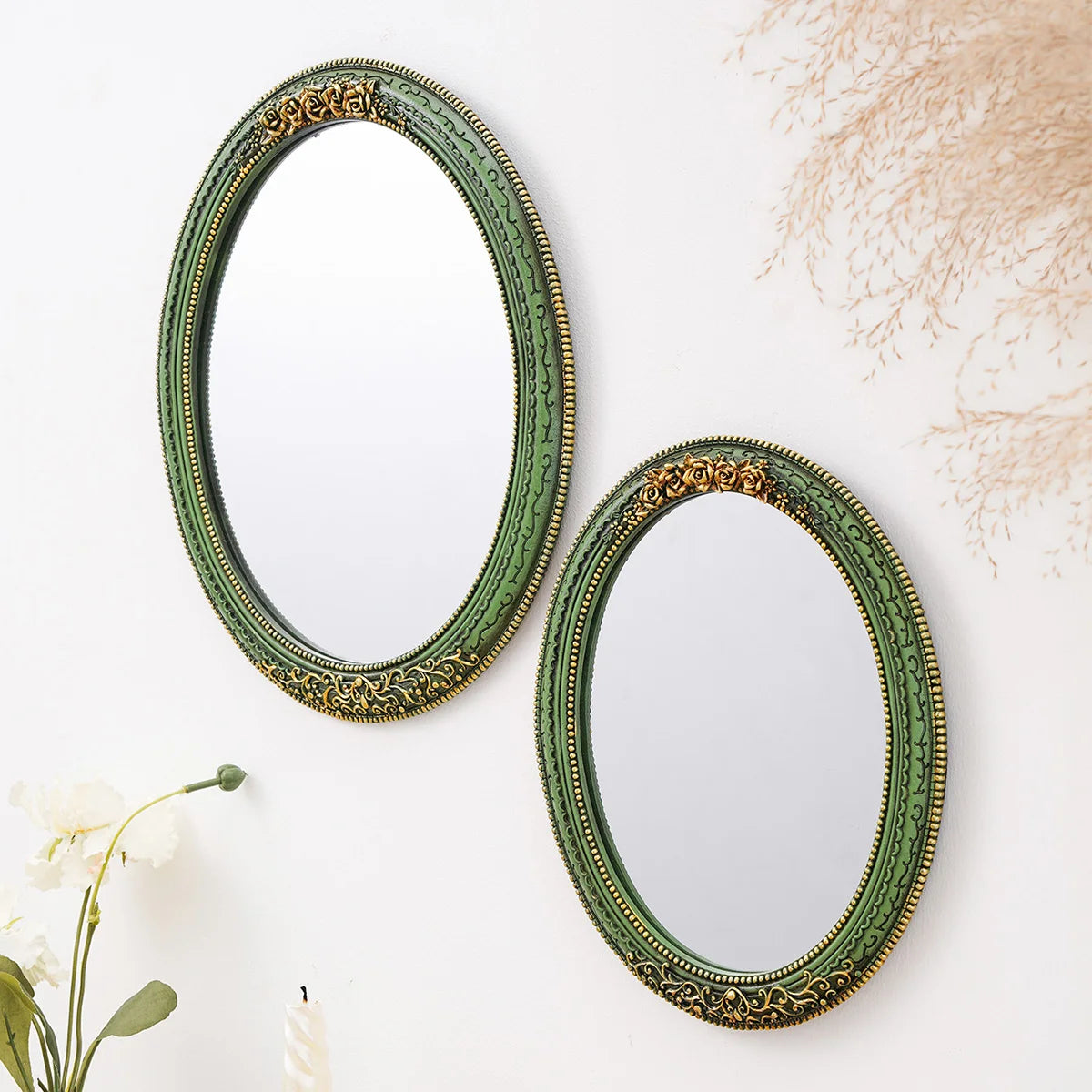 A vintage olive green oval wall mirror with an intricate gold lace design hanging on a white surface.