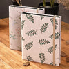 A beige linen photo album with a light green botanical pattern, resting on a wooden surface.