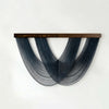 A dark blue macrame wall tapestry featuring three curved fringe elements suspended from a wooden bar.
