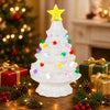 A white ceramic Christmas tree decorated with multicolor LED lights, surrounded by pine branches and wrapped gifts.