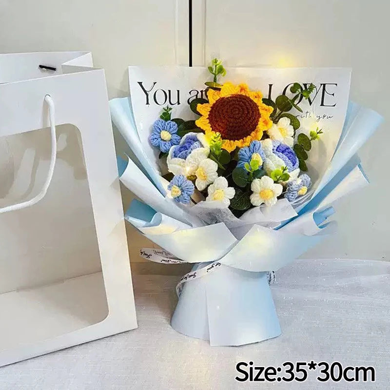 A bouquet of handmade crochet flowers featuring a large yellow sunflower and blue accent flowers, wrapped in light blue paper