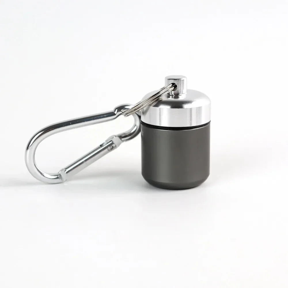 A small, silver pill organizer is attached to a metal keyring.