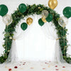 A floral arch decorated with dark green foliage and gold balloons, set against a white backdrop.