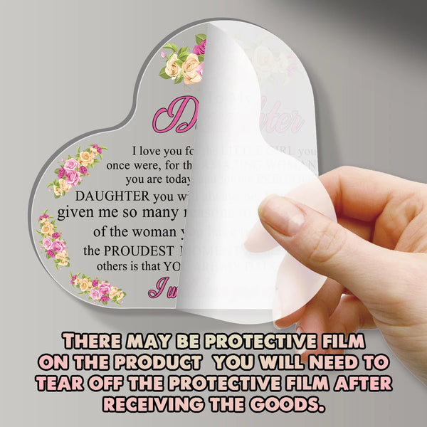 A hand holds a heart-shaped acrylic plaque with a pink floral design, showing protective film on the product.