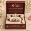 A gold and pearl charm bracelet with a red bird pendant set in a maroon box.
