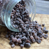 A glass jar filled with dark black salt is tipped over onto a wooden surface.