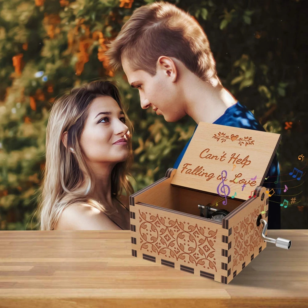 A young couple looks at a vintage hand-cranked wooden music box labeled Can't Help Falling in Love on a wooden table.