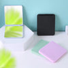 A set of compact foldable travel makeup mirrors in white, lime green, and purple are displayed on a white surface.