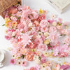 A dense arrangement of pink, peach, and cream silk artificial flower heads scattered on a white surface.