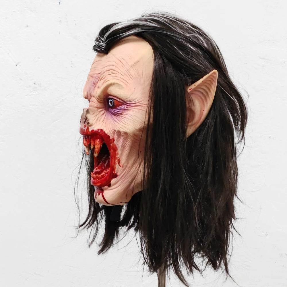 A lifelike vampire mask featuring pale skin, bloody fangs, and long black hair against a white background.