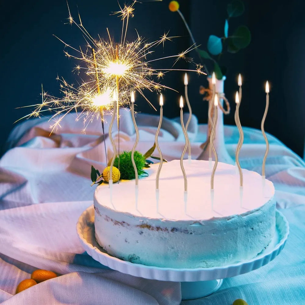 A white birthday cake decorated with blue frosting and lit candles, surrounded by sparkling golden fireworks.