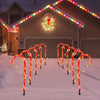 Five red and white candy cane pathway lights illuminating a snowy walkway leading to a house with a lighted gable.