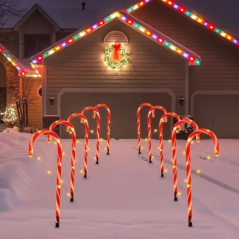 Five red and white candy cane pathway lights illuminating a snowy walkway leading to a house with a lighted gable.