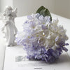 A bouquet of white and purple silk hydrangea flowers next to a white figurine.