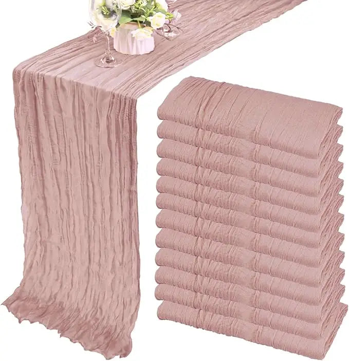 A set of ten terracotta semi-sheer cheesecloth table runners in a dusty rose color displayed on a table.