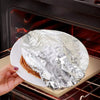 A hand holds a piece of aluminum foil covering a food item inside an oven or grill.