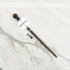 A dark wooden magic wand replica with a metal core is displayed on a white marble surface.
