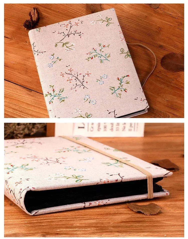 A light pink linen photo album with delicate green and pink floral embroidery resting on a wooden surface.