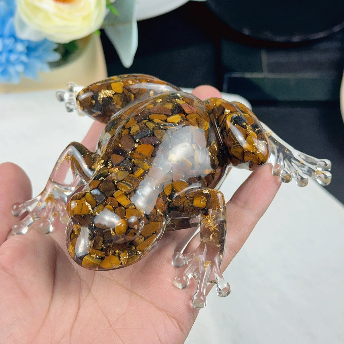 A clear resin craft decoration shaped like a frog with golden and amber inclusions is held in a hand.