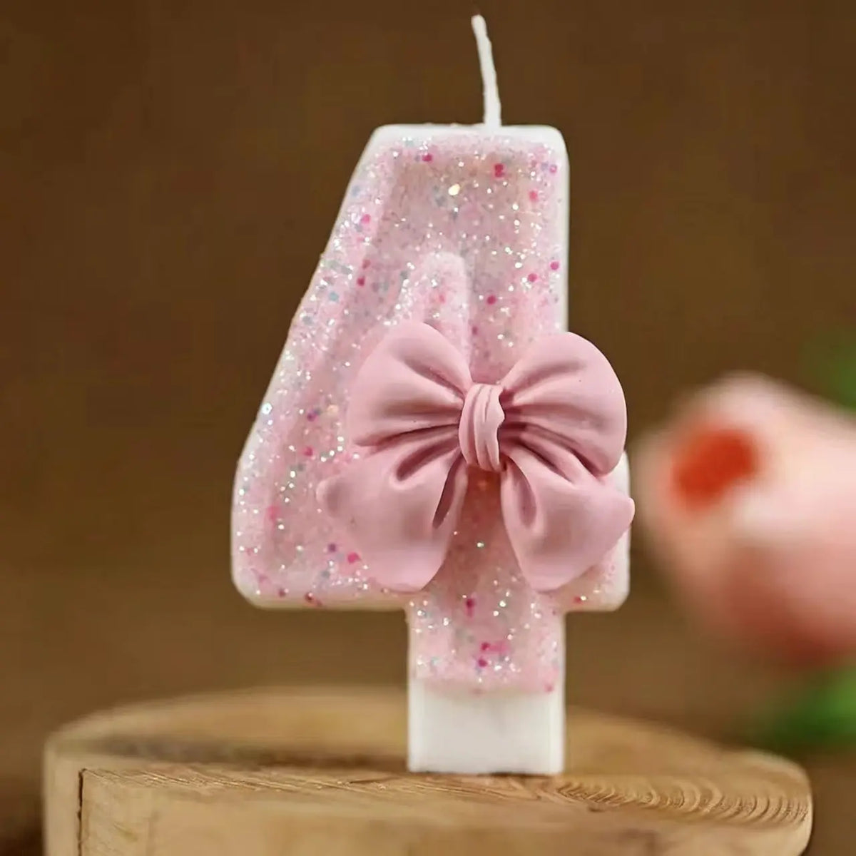 A pink glitter candle shaped like the number 4 with a bow decoration.