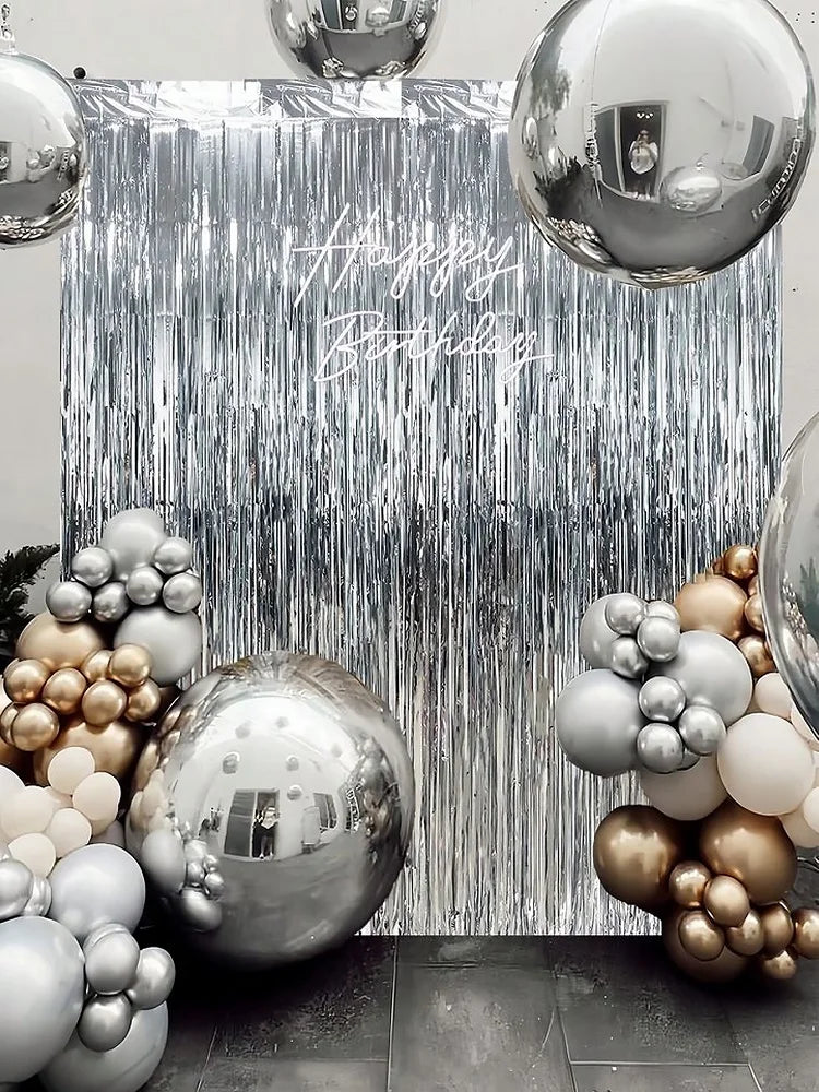 A silver and gold balloon and metallic foil fringe curtain backdrop for a birthday party.
