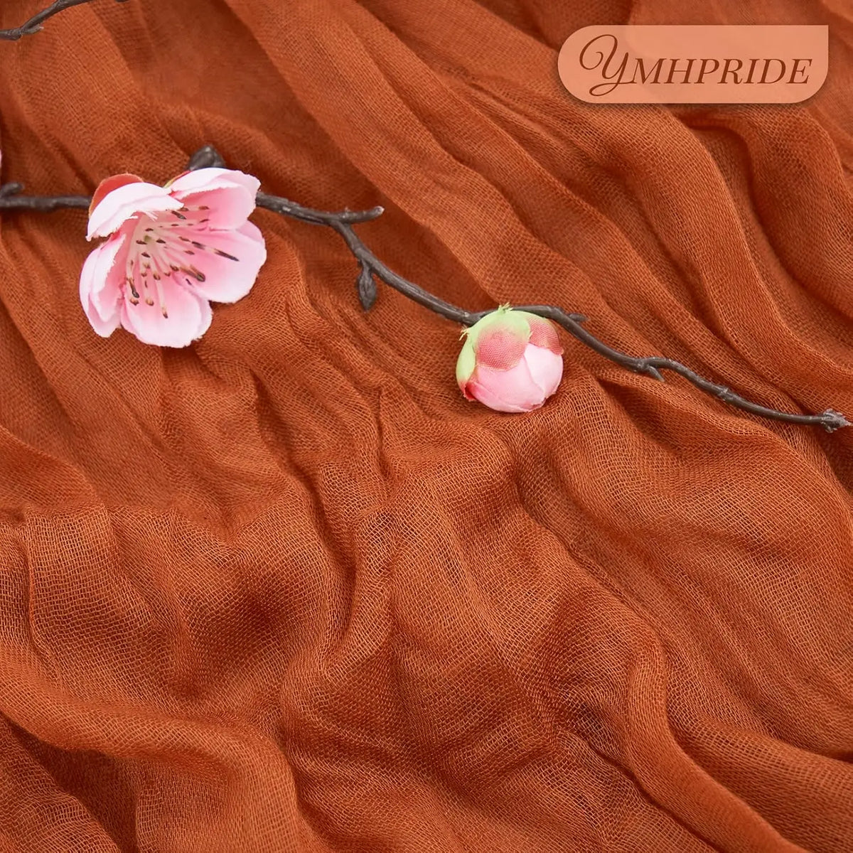 A close-up of a terracotta semi-sheer cheesecloth table runner with pink cherry blossoms and a small pink flower on a brown f