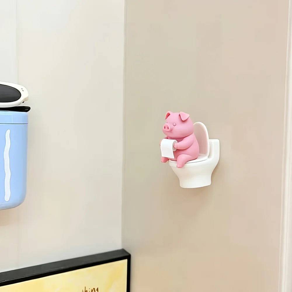 Figurine de cochon en céramique rose montée sur un porte-rouleau de papier toilette blanc sur un mur clair.