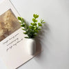 A white ceramic vase holds a sprig of bright green artificial flowers on a white surface.