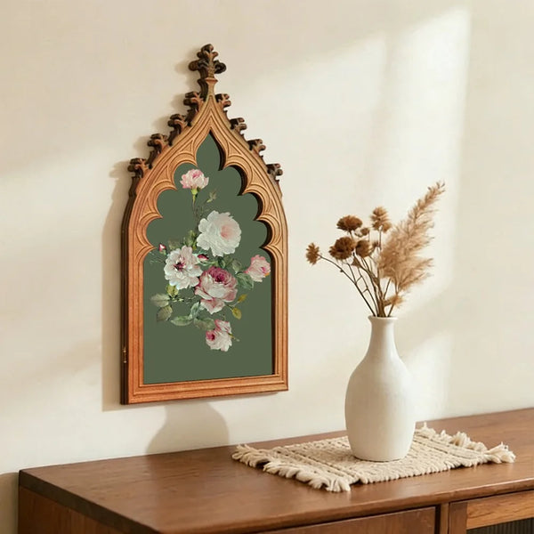 A framed antique rose finish wooden wall plaque with a pointed Gothic arch design and green foliage.