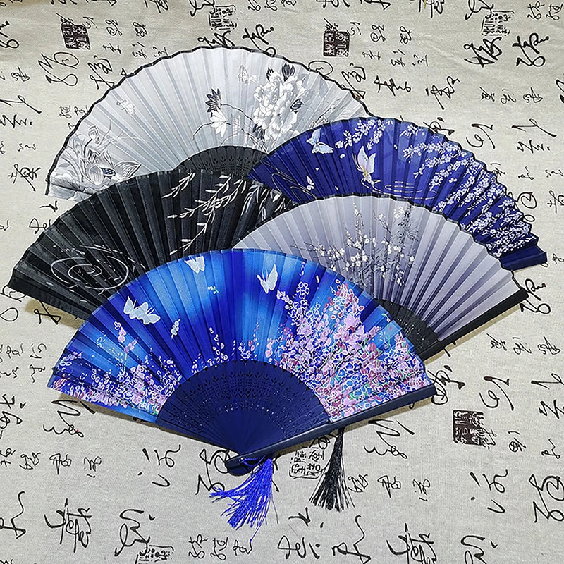 A collection of elegant vintage Chinese folding hand fans in various shades of blue and black displayed on a light patterned 