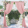 A pink chiffon backdrop curtain decorated with floral greenery and hanging crystals for a wedding or event.