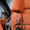 A black 10kg dumbbell is hanging from a leather car seat back organizer in an orange vehicle interior.