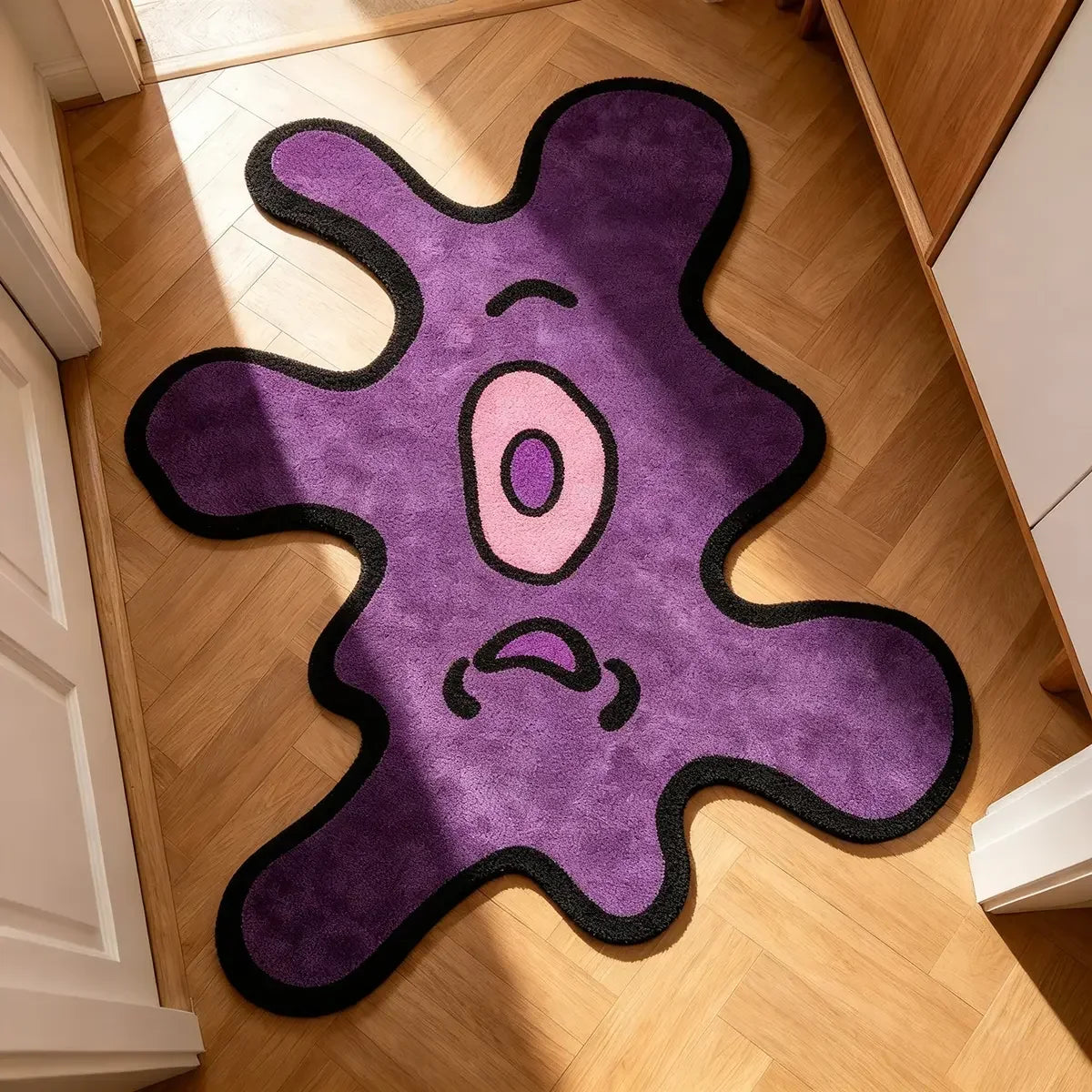 A purple cartoon monster rug with black outline and pink eyes placed on a light wood floor.